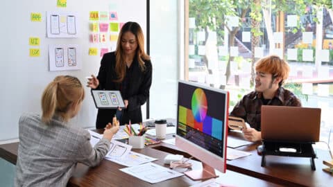 Female website designer showing user interface design on digital tablet to her web design team